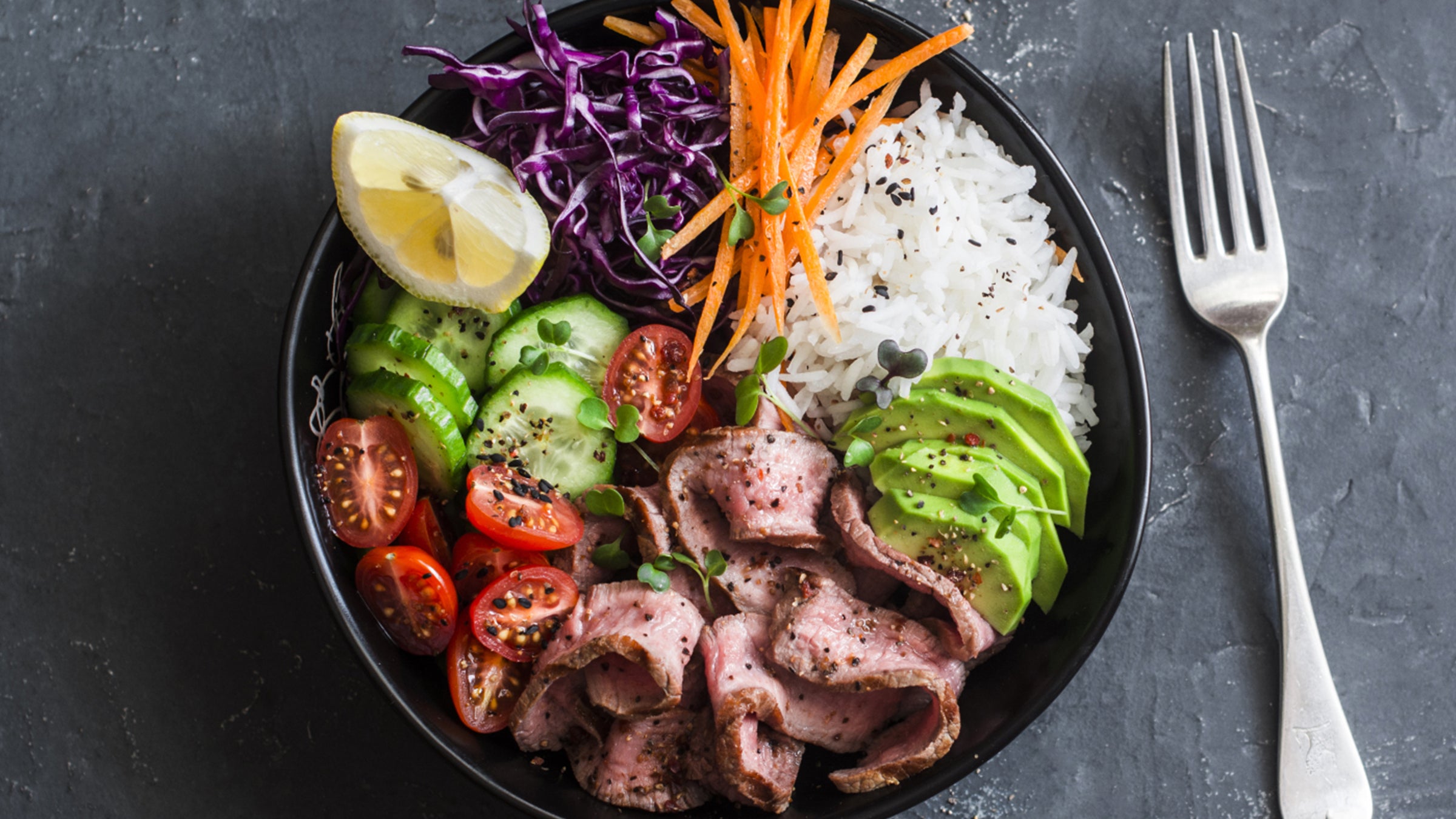 Protein and vegetable rice bowl: bowl with beef, tomatoes, cucumber, carrot, avocado, cabbage and white rice.