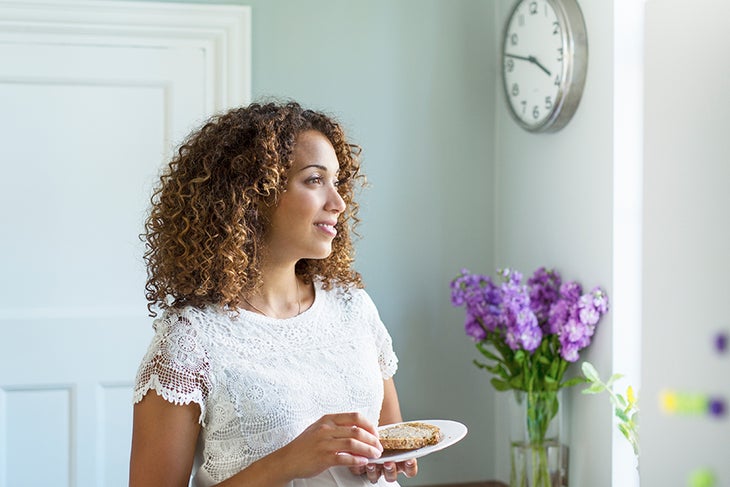 Woman eating in the kitchen near a clock