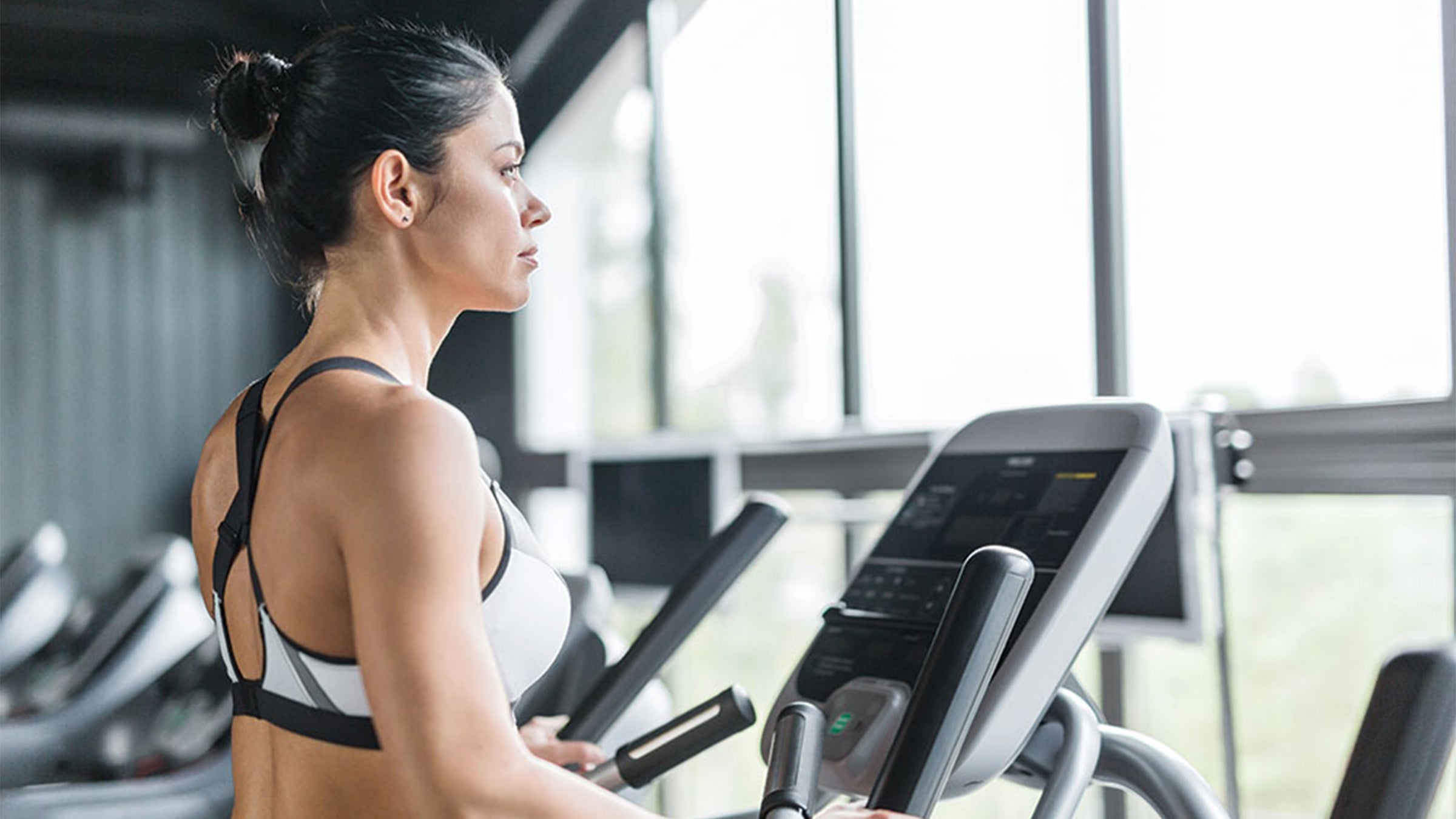 Woman in sports bra on the treadmill at the gym, looking out the window into nature.